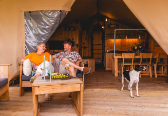Coppia che si rilassa con vino e cane sulla terrazza della Safarilodge Gazelle al Vakantiepark IJsselhof.