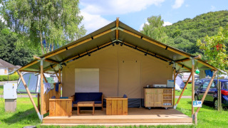 Tenda safari senza servizi igienici, arredata con mobili in legno su veranda in campeggio erboso.