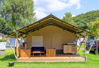 Safari tent without sanitation, furnished with wood on a deck, set on a grassy campsite under blue sky.