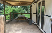 Wooden terrace with bench and canopy outside Cottage at Camping Seasonova du Chêne, surrounded by greenery.