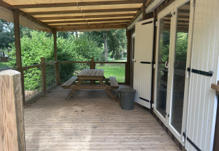 Træterrasse med bænk, overdækning og udsigt til grøn natur ved Cottage på Camping Seasonova du Chêne.