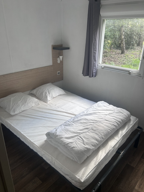 Soveværelse i Cottage på Camping Seasonova du Chêne i Frankrig med dobbeltseng, vindue og naturudsigt.