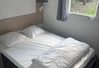 Soveværelse i Cottage på Camping Seasonova du Chêne i Frankrig med dobbeltseng, vindue og naturudsigt.