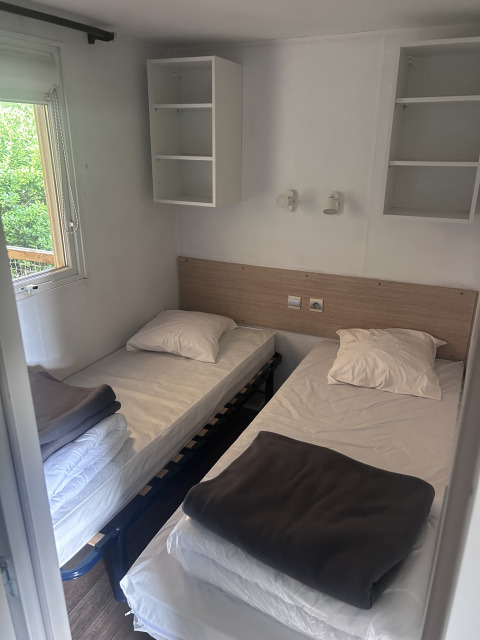 To enkeltsenge med hvide lagner og grå tæpper på et værelse på Cottage at Camping Seasonova du Chêne i Frankrig.