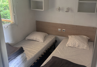 To enkeltsenge med hvide lagner og grå tæpper på et værelse på Cottage at Camping Seasonova du Chêne i Frankrig.