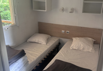 Two single beds with white linens and gray blankets in a room at Cottage at Camping Seasonova du Chêne, France.