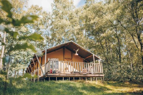Safari-Zelt auf einer Holzterrasse im Grünen, von Bäumen umgeben, perfekt für ein Naturerlebnis.