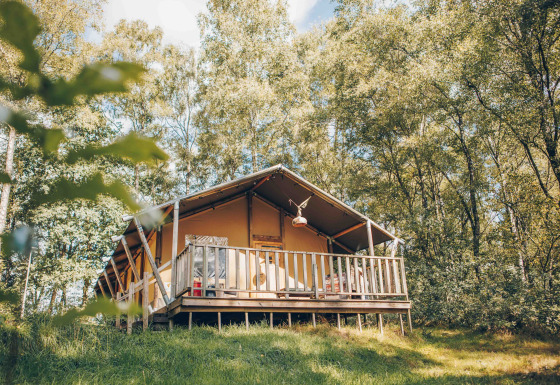 Safari-Zelt auf einer Holzterrasse im Grünen, von Bäumen umgeben, perfekt für ein Naturerlebnis.