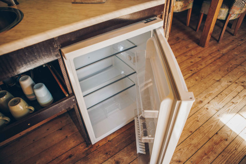 Offener Mini-Kühlschrank mit leeren Regalen in einem Safarizelt am Wilsumer Berge, Deutschland, Holzboden.