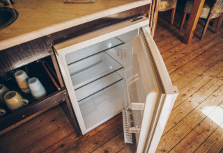 Offener Mini-Kühlschrank mit leeren Regalen in einem Safarizelt am Wilsumer Berge, Deutschland, Holzboden.