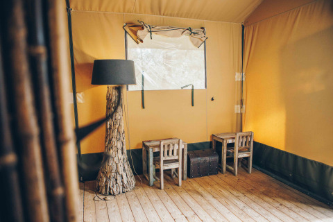 Innenansicht eines Safari-Zeltes bei Wilsumer Berge in Deutschland mit Holzstühlen und rustikaler Lampe.