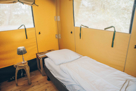 Indvendigt af en safariteltseng med enkeltseng, træbord og lampe på Wilsumer Berge i Tyskland.