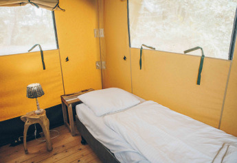 Indvendigt af en safariteltseng med enkeltseng, træbord og lampe på Wilsumer Berge i Tyskland.