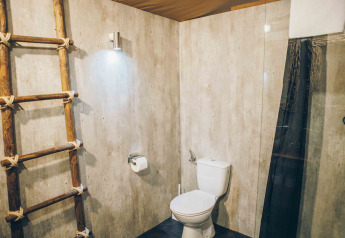 Moderne badeværelse med trægulv, stige, toilet og minimalistisk belysning i en safariteltsuite.