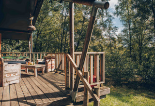 Træterrasse ved en safaritelte på Wilsumer Berge i Tyskland med rustikke møbler i skovomgivelser.