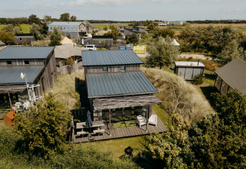 Vista aerea del lodge Juttershut con cabine in legno moderne, prati verdi e paesaggio rurale circostante.