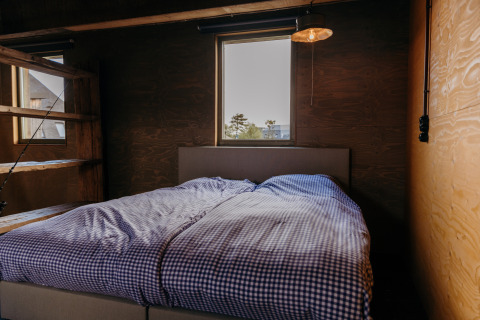 Bedroom inside Juttershut lodge at Duynpark Het Zwanenwater in the Netherlands, featuring checkered bedding and wood walls.