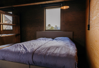 Chambre dans la cabane Juttershut au Duynpark Het Zwanenwater, Pays-Bas, avec linge de lit à carreaux et murs en bois.