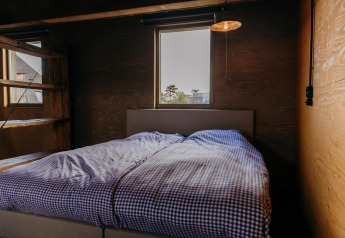 Chambre dans la cabane Juttershut au Duynpark Het Zwanenwater, Pays-Bas, avec linge de lit à carreaux et murs en bois.