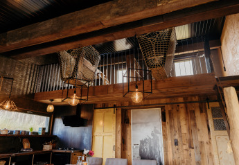 Intérieur rustique du lodge Juttershut à Duynpark Het Zwanenwater avec mezzanine en filet et détails bois.