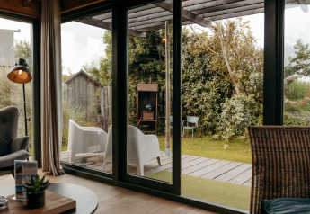 Vista dal soggiorno attraverso grandi porte in vetro su terrazza e giardino a Juttershut, Duynpark Het Zwanenwater, Paesi Bassi.