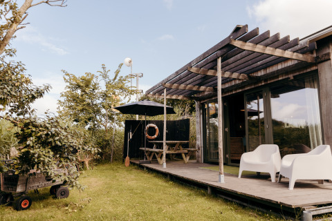 Buitenzicht op lodge Juttershut bij Duynpark Het Zwanenwater in Nederland met veranda en tuinmeubilair.