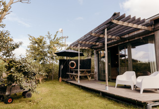 Buitenzicht op lodge Juttershut bij Duynpark Het Zwanenwater in Nederland met veranda en tuinmeubilair.