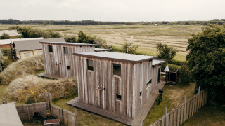 Two wooden lodges at Juttershut, Duynpark Het Zwanenwater, Netherlands, surrounded by open grassy fields.