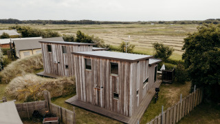 Two wooden lodges at Juttershut, Duynpark Het Zwanenwater, Netherlands, surrounded by open grassy fields.
