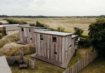 Dos cabañas de madera en Juttershut, Duynpark Het Zwanenwater, Países Bajos, rodeadas de campos abiertos.