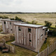 Due lodge in legno a Juttershut, Duynpark Het Zwanenwater, Paesi Bassi, circondati da campi aperti.
