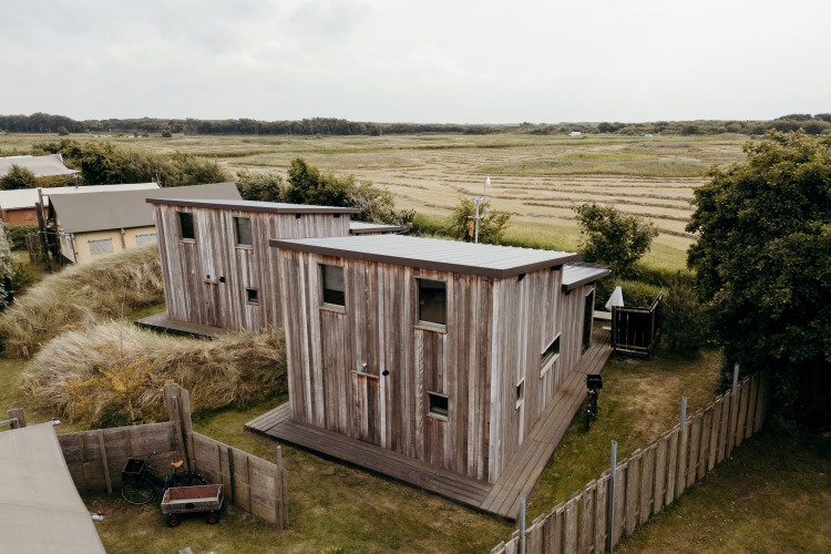 Zwei mit Holz verkleidete Lodges im Duynpark Het Zwanenwater, Niederlande, mit Feldern im Hintergrund.