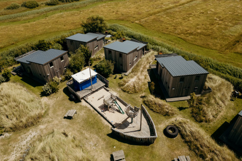 Luchtfoto van huisjes en een speelplaats in de vorm van een schip bij Juttershut lodge, Duynpark Het Zwanenwater.