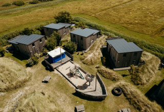 Luchtfoto van huisjes en een speelplaats in de vorm van een schip bij Juttershut lodge, Duynpark Het Zwanenwater.