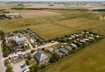 Aerial view of a glamping site with modern tents, expansive green fields, and rural buildings nearby.