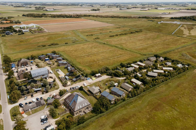 Vista aérea de un alojamiento glamping con tiendas modernas, extensos campos verdes y edificios rurales.