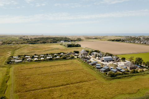 Luchtfoto van een glamping met tenten en cabines op het platteland, omringd door natuur en velden.