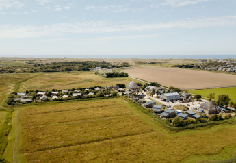 Aerial view of a countryside glamping site featuring tents, cabins, and open fields under a blue sky.