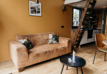 Sala de estar en Rescue cottage de Duynpark Het Zwanenwater, con sofá marrón, escalera y cocina.
