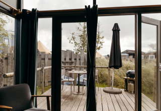 Blick aus einem Tiny House im Duynpark Het Zwanenwater, Niederlande, auf Terrasse mit Stühlen und Sonnenschirm.