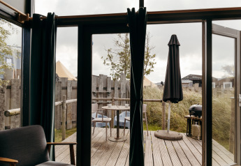 Vista desde una tiny house en Duynpark Het Zwanenwater, Países Bajos, con terraza, sillas y sombrilla negra.