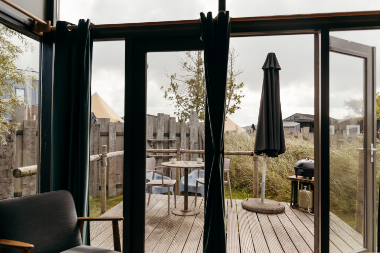 Vista desde una tiny house en Duynpark Het Zwanenwater, Países Bajos, con terraza, sillas y sombrilla negra.