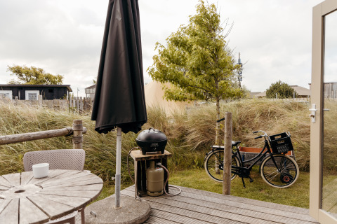 Wooden patio with table, chairs, black umbrella, grill and bicycle outside Rescue cottage at Duynpark Het Zwanenwater.