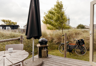 Holzterrasse mit Tisch, Stühlen, Grill und Fahrrad vor einem Tiny House im Duynpark Het Zwanenwater, Niederlande.