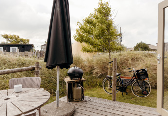Terrasse en bois avec table, chaises, parasol noir, barbecue et vélo près du Rescue cottage à Duynpark Het Zwanenwater.
