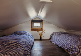 Grenier chaleureux avec deux lits simples et literie à carreaux au Rescue cottage de Duynpark Het Zwanenwater.