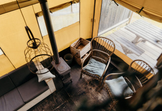 Interior view of a safari tent with wooden chairs, stove, and outdoor picnic table at Duynpark Het Zwanenwater.