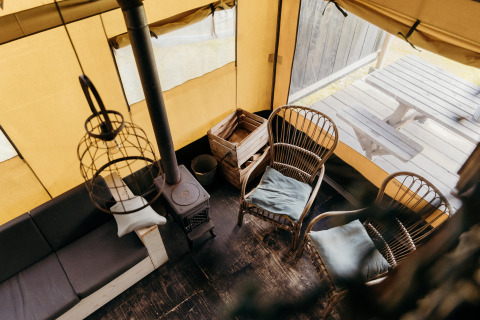 Vista interior de una tienda safari con sillas de madera, estufa y mesa de picnic exterior en Duynpark Het Zwanenwater.