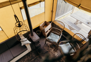 Vista interior de una tienda safari con sillas de madera, estufa y mesa de picnic exterior en Duynpark Het Zwanenwater.
