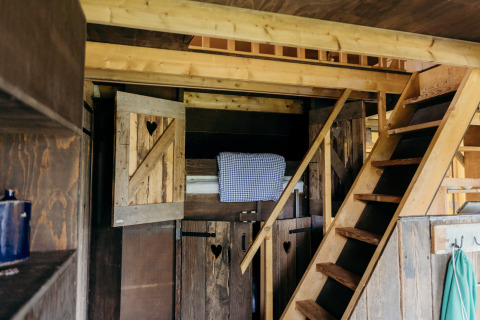 Interior of a rustic cabin with wooden loft, stairs, and bed at Wood Lodge, Duynpark Het Zwanenwater in the Netherlands.